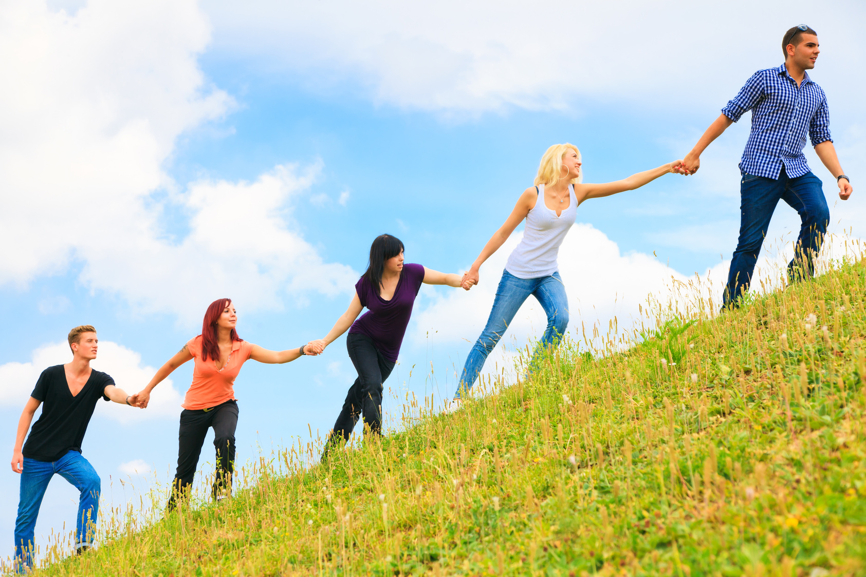 young people helping each other climb a hill